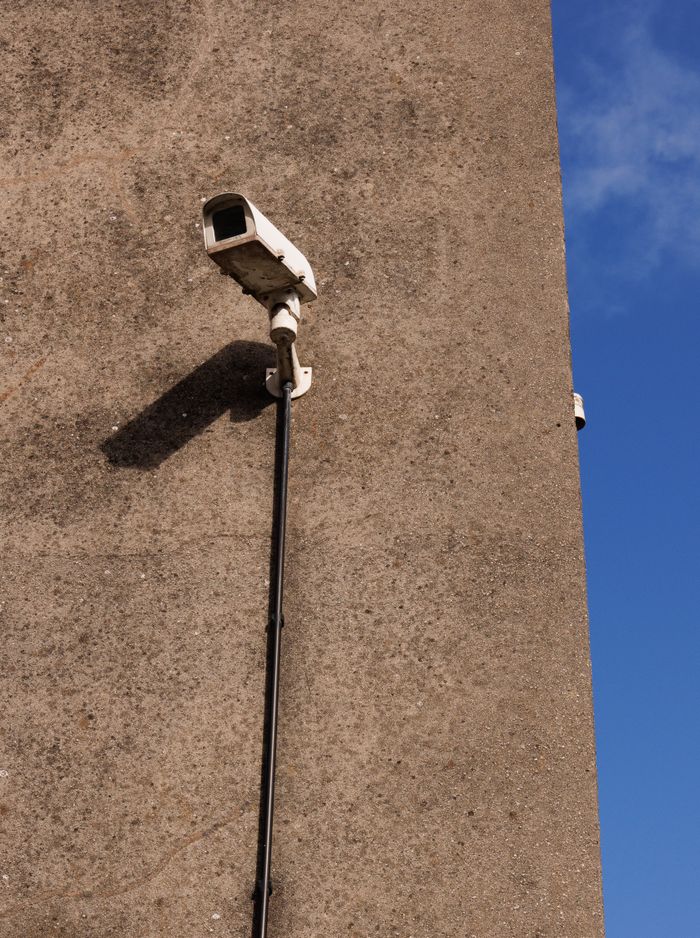 A security camera fixed on a concrete wall under a clear blue sky.