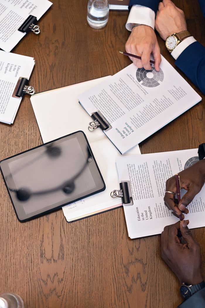 gallery-02 Top view of a business meeting with hands, tablets, and documents on a table.